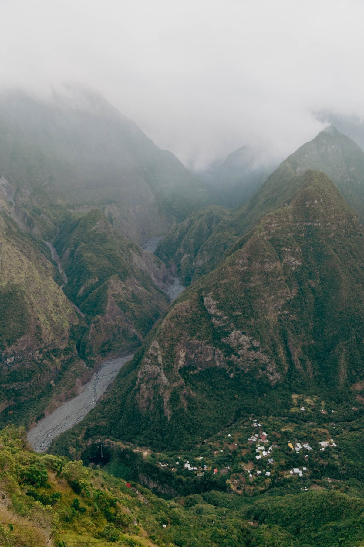 Steep green mountains and a small village in a valley, with mist over the peaks, Reunion Island